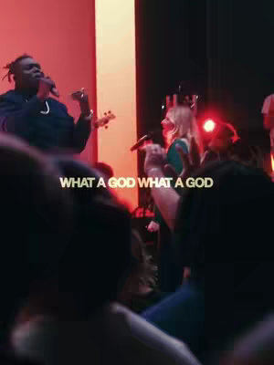A live performance scene featuring a band and singers, the front is obscured to a partial view. Text overlayed: 'WHAT A GOD'.