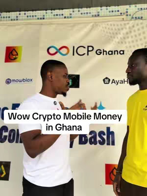 Two men are standing side by side and facing left, appearing to be engaged in a conversation. The man on the left is wearing a white t-shirt and is gesturing with his hands. The man on the right is wearing a yellow t-shirt. Behind them is a backdrop with logos and text. Overlaid on the image is a white rectangular box with the text "Wow Crypto Mobile Money in Ghana".