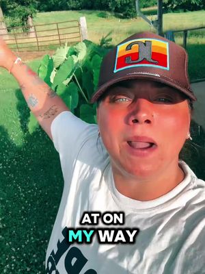 A woman wears a hat and white top, facing the camera. The image has a natural green background. Text overlayed on the bottom.