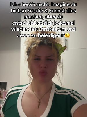 A selfie-style image featuring a young woman in a green and white striped top. She has light skin, blonde hair styled up with a green flower accessory. She is making a pouting face. In the background, there is a plain white wall.