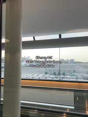 The image captures a view through a window, likely at an airport, showcasing an airplane on the tarmac in the background. Text overlays the scene, stating a bible verse.