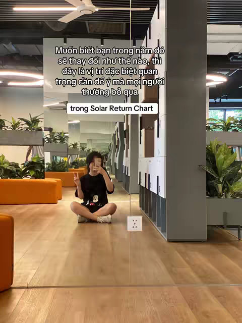 A woman is sitting cross-legged on a wooden floor, taking a selfie with her phone. She is in a well-lit room with tall gray cabinets and what appears to be a gym or office setting. Text overlay is added to the image, providing context to the video's subject.