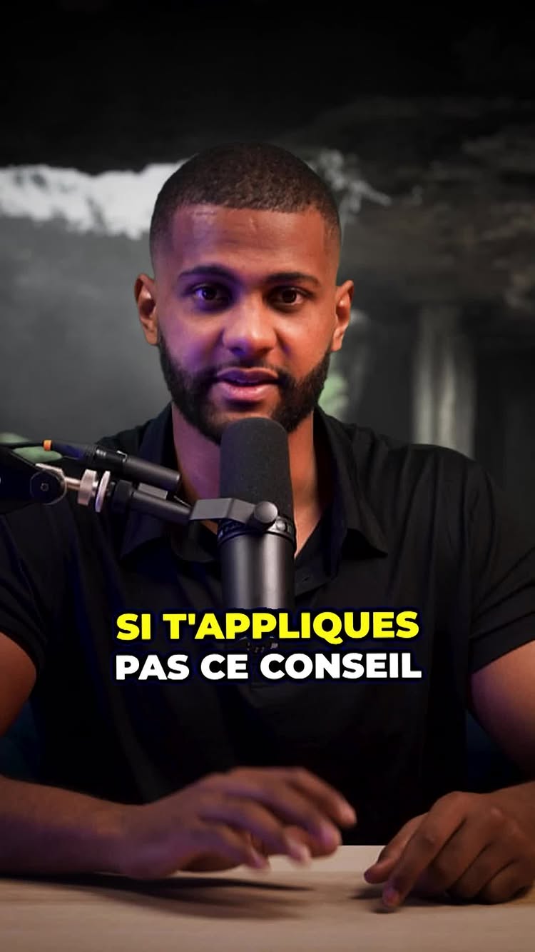 The image features a man in a studio setting. He is positioned in the center, facing the camera with a neutral expression. A microphone is placed directly in front of him. The background is blurred. Across the bottom, a yellow box displays the text overlay in French.