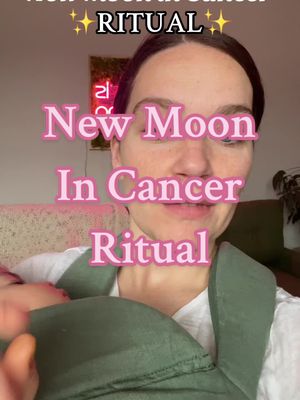 A woman in a white shirt and a green baby carrier is holding a baby. The background has a pink wall and a piece of art on the wall. Text overlays the woman, with the words 'New Moon In Cancer Ritual'.
