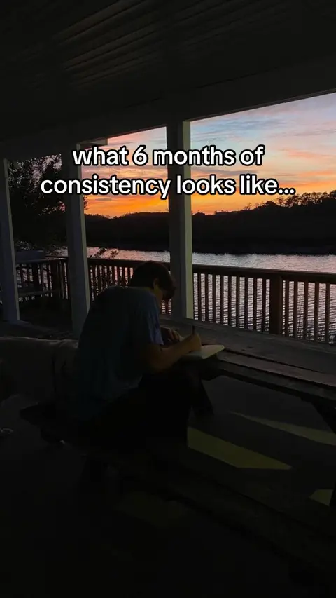 The image shows a person writing at a wooden table on a porch. The sky is filled with vibrant colors of a sunset with pinks, oranges, and yellows. Outside the porch is dark, with a body of water in the background. The text overlay appears in the upper center.