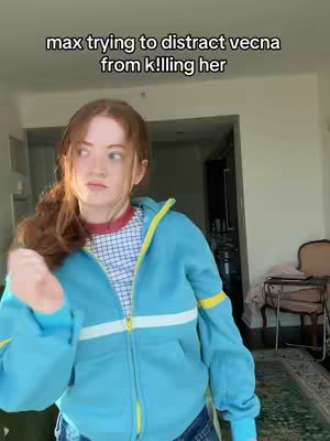 The cover image features a young woman cosplaying as the character Max Mayfield from the show Stranger Things. She is in a room with neutral colored walls and appears to be holding her hand out slightly, partially obscuring her face with a concerned or focused expression. Above her head is text, reading 'max trying to distract vecna from killing her'. She wears a blue jacket and a red shirt with white dots.