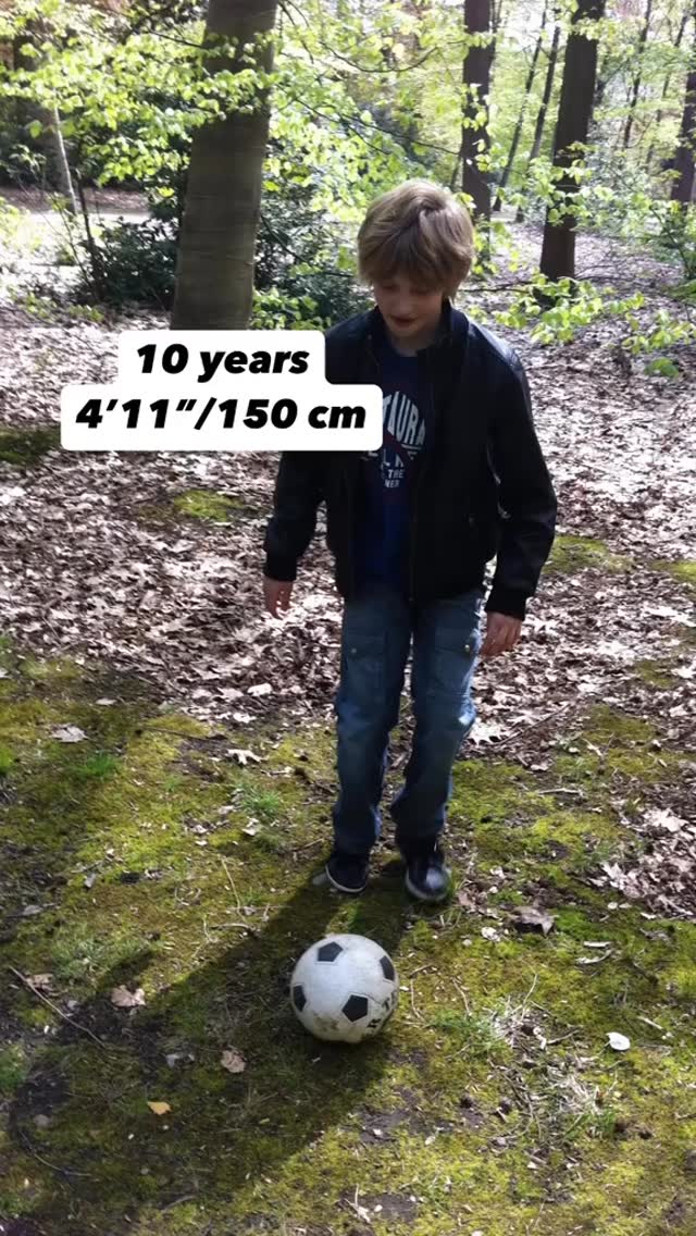 A young boy standing in a forested area, next to a soccer ball. The boy is wearing a black jacket, blue jeans, and sneakers and has text overlayed on the image displaying his age and height.