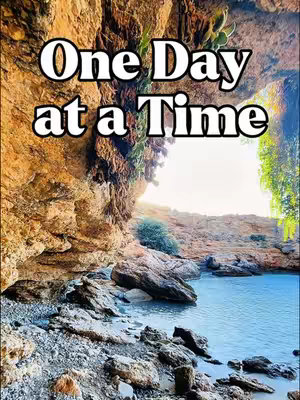 The cover image shows a hidden beach scene through a cave opening. The opening in the rock reveals a bright sky and the blue water of the ocean. The text 'One Day at a Time' is overlaid in a white, stylized font.