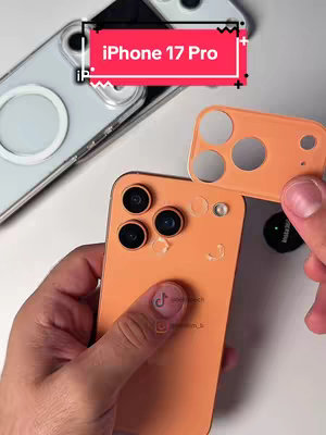 The cover image shows a person's hands holding a mockup of a future iPhone design. The phone itself is orange, with visible camera lenses and design elements, alongside an orange camera lens module detached from the phone. Other devices, including a white iPhone, are partially visible in the background. The lighting appears to be artificial and direct, highlighting the details of the mockup. The background provides a bright, uncluttered setting, emphasizing the focus on the phone and its features.