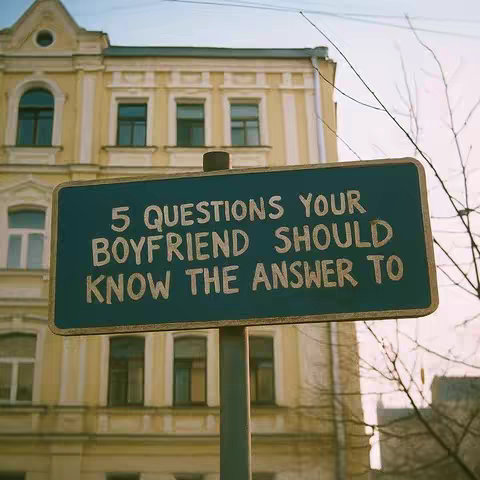 The image showcases a blue sign against a blurred background of a building with yellow walls and multiple windows. The sign reads, "5 QUESTIONS YOUR BOYFRIEND SHOULD KNOW THE ANSWER TO" in white text.
