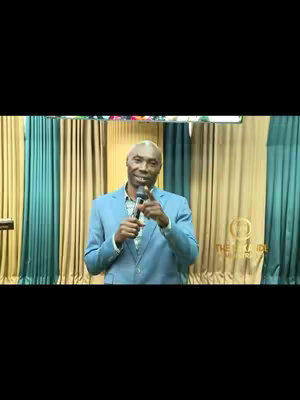 The video features a man in a blue suit standing in front of a stage, holding a microphone and speaking. Behind him are green and gold curtains and a sign that appears to be a logo.