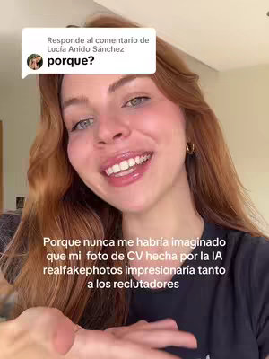 A young woman with long, wavy auburn hair smiles broadly at the camera, appearing in a selfie-style video. She's wearing gold hoop earrings and a black t-shirt. Behind her, the background is brightly lit, with warm, neutral tones. A text overlay is present, appearing as a speech bubble on top of the woman's head. There's a text at the bottom of the image.