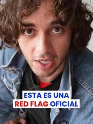 A close-up shot of a young man with curly brown hair. He is looking directly at the camera, and his mouth is slightly open as if he is speaking. He is wearing a denim jacket over a black t-shirt. A graphic overlay displays the words "ESTA ES UNA RED FLAG OFICIAL" in a bold white font with a red flag icon. The background is blurred, drawing focus to the man and the text overlay.