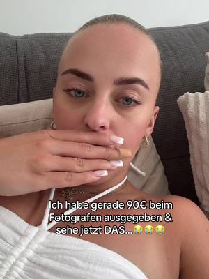 A selfie shows a woman with fair skin, light blue eyes, and blonde hair pulled tightly back, covering the top of her head. The woman's left hand is raised to cover her mouth, revealing manicured fingernails. Text overlaid on the image indicates that the woman spent 90 euros on a photographer and is surprised by the result, showing an emotion of shock.