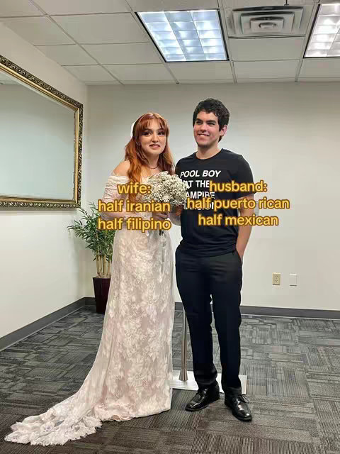 A wedding photo featuring a bride in a lace gown and a groom in a black t-shirt and dress pants. Text overlays identify the bride's and groom's ethnicities.