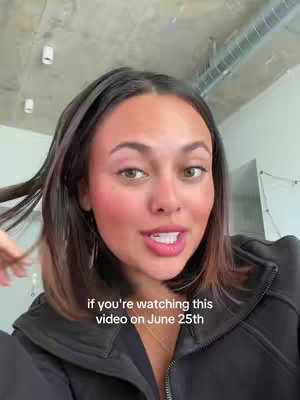 A woman with brown hair is shown from the chest up, speaking directly to the camera against a blurry indoor backdrop. She has fair skin, medium brown hair, and is wearing a black jacket. The image has a warm tone, with the focus on her facial expression and the text overlay.
