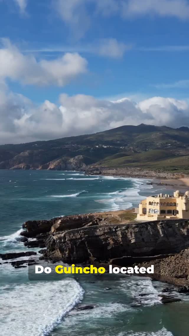 A coastal landscape with a yellow building situated on a rocky promontory, featuring a beach and ocean under a blue sky with clouds. Text overlay highlights 'Do Guincho located.'