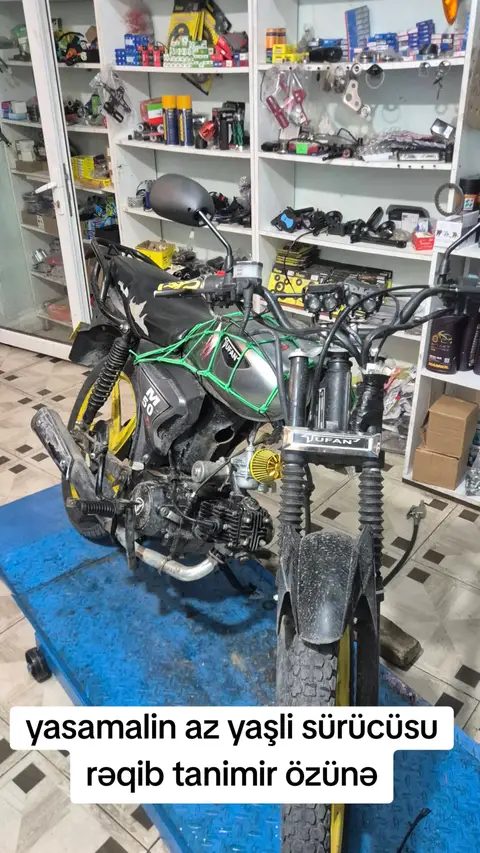A motorcycle is parked on a blue platform, with an open repair shop background. The motorcycle is black and yellow. The text overlay is in a white box at the bottom.
