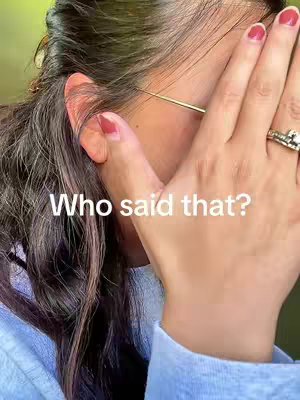 A close-up shot of a person partially covering their face with their hand. The person is wearing glasses and has their hand up to their mouth, nails are painted red. Text overlayed on the image says: "Who said that?"