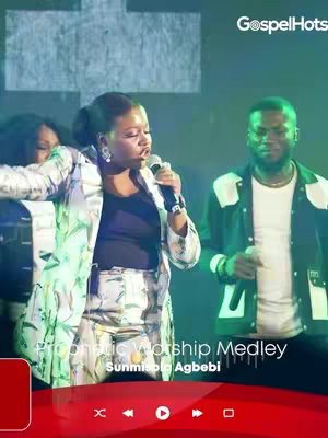 The cover image features a live performance setting. A woman is centered, singing into a microphone, wearing a patterned blazer and a black top. Behind her are two other people, one is wearing glasses, appearing to be male. The background has stage lighting, setting a lively atmosphere.