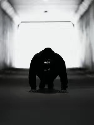 A black and white photo shows a person on their hands and knees in the center of a tunnel. The person is wearing a black hoodie, obscuring their features. The tunnel's opening is brightly lit.