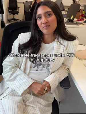 A woman in a white striped blazer and t-shirt sits in an office setting, facing the camera. Text overlaid on the image reads, "Affordable fragrances under £70 to shop now."
