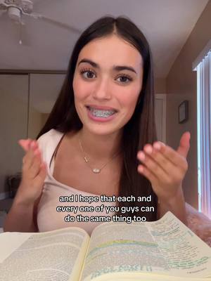 A young woman with dark hair, braces, and a pink top smiles at the camera, hands gesturing outwards, with an open Bible in front of her and text overlayed that reads, "and I hope that each and every one of you guys can do the same thing too". The background shows a room.