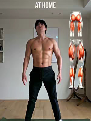 A man with a muscular physique stands shirtless in a home environment, with black pants providing contrast to his toned torso. The background is a neutral-toned room with exercise diagrams and “AT HOME” text superimposed.