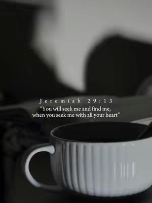 A grayscale image featuring a white mug with a dark interior and a textured surface, set against a soft, blurred background. Text overlays are positioned above the mug, displaying a biblical verse.