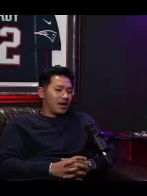 A person, likely the creator, is seated in a casual interview setting. They're positioned in front of a framed jersey hanging on the wall, and a microphone to their right. The lighting is dim with a mix of cool and ambient tones.