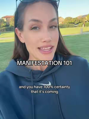 The cover image shows a woman in her thirties or forties, with long, dark hair and sunglasses on her head. She's wearing a dark blue hoodie in a natural setting, likely a park, with green grass and trees in the background. The main focus is the woman, who appears to be speaking or smiling. Overlayed on the image is the text 'MANIFESTATION 101' in white.
