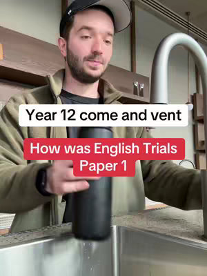 A man wearing a black baseball cap and a green jacket, appearing to be in a kitchen or a similar setting with a stainless steel sink and tap. He is holding a black water bottle as if he is about to put it under the tap. Two text overlays in white and red boxes state the video question and prompt: "Year 12 come and vent", and "How was English Trials Paper 1".