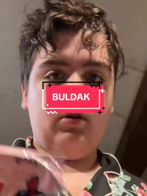 A close-up shot of a person's face, with the focus on the upper half. The person has short, dark, curly hair and is looking directly at the camera. The hook of the video is a colored banner, inside of which is written the word: BULDAK.