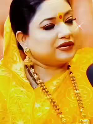 A medium shot featuring a woman facing slightly to the side, presenting a serene expression.  She's wearing a yellow ensemble, adorned by golden jewelry and a red mark on her forehead. The overall lighting is soft, enhancing the warmth and complexion of her skin.