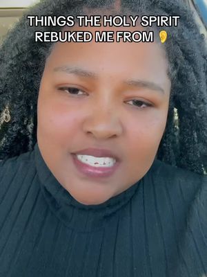 A selfie-style shot featuring a Black woman with curly hair smiling slightly at the camera. The top of a black turtleneck is visible, and the image has an overall warm tone, lit from the front.