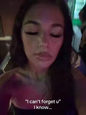 A selfie-style shot with a woman facing the viewer with closed eyes. The background is blurred, suggesting a dark or indoor setting. Overlayed text appears at the bottom: "I can't forget u" followed by "I know...". The lighting gives a pinkish hue to the scene.