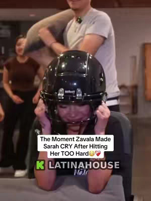 A woman in a football helmet is shown from the chest up, covering her face with her hands and appearing to cry. Behind her, a man holds a padded object, and another woman is visible in the background. The text overlay indicates that someone named Zavala made Sarah cry.