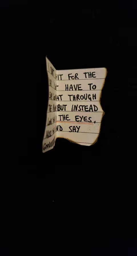 A black background with a torn piece of paper in the center. The paper has handwritten lines of text with parts burned off. The text includes the phrases "I can't wait", "have to", and "the eyes, and say."