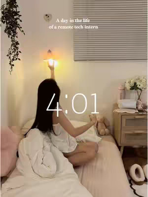 A woman sits cross-legged on a bed, illuminated by soft light. A digital clock displays '4:01' in white at the center. The woman reaches up to touch a bedside lamp, a teddy bear rests nearby, and floral arrangements and accessories adorn the nightstand. Background includes a shuttered window and leafy vines hanging from the wall.
