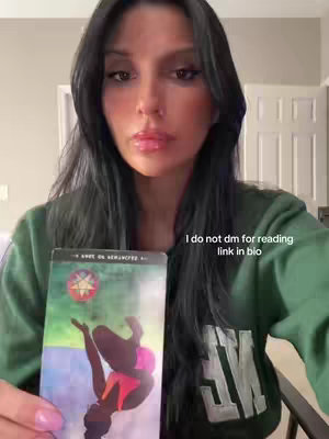 A woman with long black hair holds a tarot card, the image is a close-up shot; overlayed text on the image informs the viewer to link in bio for readings.