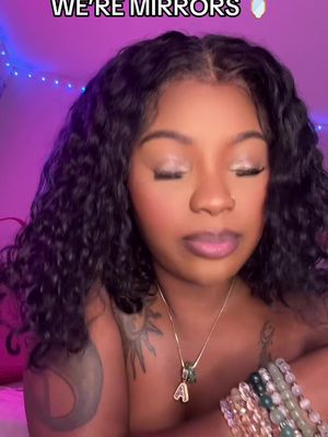 A close-up shot of a woman with dark, curly hair. She has closed eyes and appears to be deep in thought. She is wearing a gold necklace with a pendant. The background has a purple hue with a few decorative lights visible, adding a soft glow to the image.