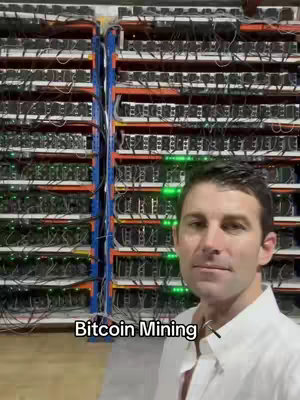 A man in a white button-down shirt stands in front of servers with intricate wiring and flashing lights. The setup resembles a data center.