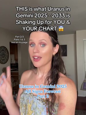 A selfie-style video cover features a woman in front of a softly lit background. Text overlays at the top announce the topic: "THIS is what Uranus in Gemini 2025 - 2033 is Shaking Up for YOU & YOUR CHART." Below, a portion of the image includes smaller notes such as "Part 2/3 Parts 1 & 3 live on my page" as well as the title "Uranus in Gemini 2025 All Signs Forecast Part 2". The woman is centered and smiling with her hand pointing upwards. Her attire is a strapless top, and she has makeup and partially up-swept hair. The image is well-lit and composed with a focus on the speaker.