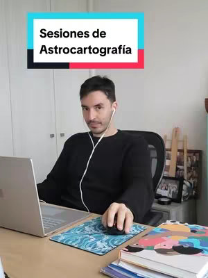 A man is seated at a desk with a laptop and mouse, wearing a black sweater and earbuds, against a white background and in front of a window. Overlayed on the image is a rectangular box with the text "Sesiones de Astrocartografía".