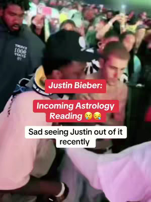 The cover image shows a crowd, with the focus on three individuals. In the foreground, a person wearing a light pink shirt and a white wrist band is partially visible. Next to him, a person wearing a baseball cap and a yellow and white striped collar is looking down. To his right, is Justin Bieber, looking down as well, with a blurred background. A red rectangular overlay with white text, that reads 'Justin Bieber: Incoming Astrology Reading', with face emojis, and the text 'Sad seeing Justin out of it recently' is overlaid.