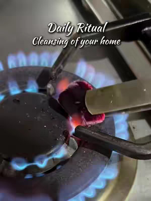 A close-up shot of a gas stove during a daily ritual. The frame focuses on the lit burner with blue flames, a metal tool is held over flames. The text overlay states 'Daily Ritual Cleansing of your home'.