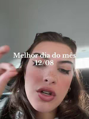 A selfie-style shot featuring a woman with long brown hair, styled with a part in the middle, and wearing sunglasses on her head. The background is blurred, suggesting she's indoors, possibly in a car. overlaid text indicating "Melhor Dia do mês 12/08". 