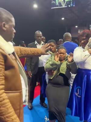 The cover image shows a group of people inside what appears to be a church. A man is standing near the left edge of the frame, with his arm outstretched towards a woman in the center. The woman is in a praying position with her eyes closed. Several other people are in the background.