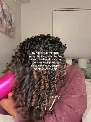 A woman is seen with her head bent down, her curly hair being blown by a pink hair dryer. Text overlays the image, partially obscured by the hair.