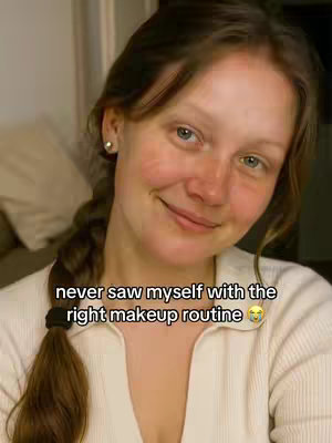 A selfie-style shot featuring a young woman with brown hair styled into a braid, wearing a white shirt. She is positioned slightly off-center, with her face taking up much of the frame. "never saw myself with the right makeup routine" is added as text on the image.
